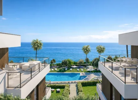 Modern apartments with terraces overlooking the sea, pool and palm trees on a sunny summer day by the coast.