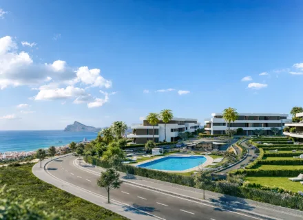 Modern coastal residences with pool, terraced gardens and palm trees overlooking the sea on a sunny summer day.