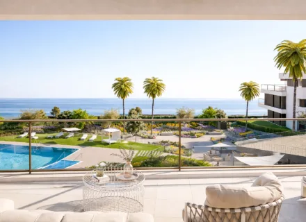Sea view from modern terrace overlooking pool, palm trees and landscaped gardens on a bright summer afternoon.