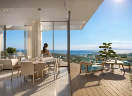 Elegant apartment interior with floor-to-ceiling windows, dining area and terrace overlooking the sea and coastline.