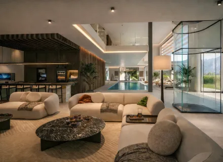 Luxury open-plan living area with designer sofas, indoor swimming pool, modern kitchen, ambient lighting and garden views.