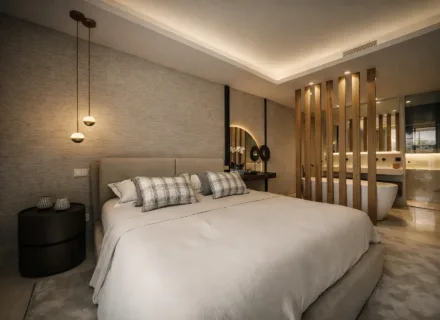 Stylish modern bedroom with upholstered bed, pendant lights, wooden details and open en-suite bathroom with bathtub.